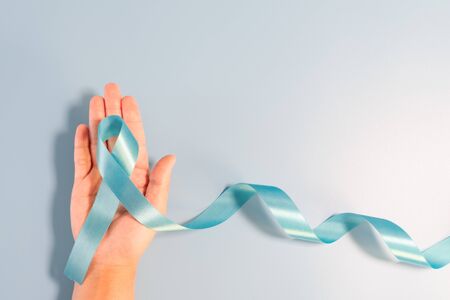 Prostate cancer awareness campaign concept, Men's health concept. hand holding light blue ribbon long tail on blue background. Symbol for support men who living with cancerの写真素材