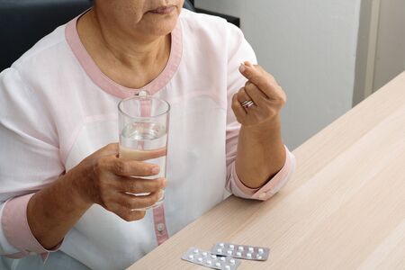 headache old women hand hold medicine with a glass of water, feeling stress, migraine, health problem conceptの写真素材