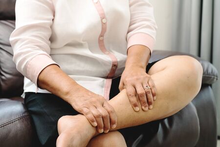 leg cramp, senior woman suffering from leg cramp pain at home, health problem conceptの写真素材