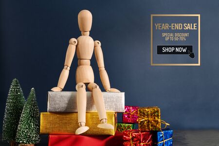 Year-End sale, wooden doll sitting on gift box with christmas treeの写真素材