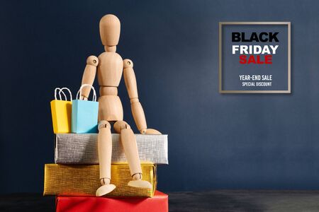 Black Friday sale, wooden doll sitting on gift box with shopping bagの写真素材