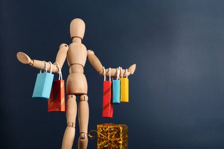 Cheerful happy shopaholic wooden doll with lots of shopping bags on armの写真素材