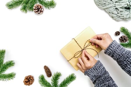 Christmas winter composition. Woman hands wrapping Christmas gifts box with pine cones, fir branches on white background. Flat lay, top view, copy spaceの写真素材