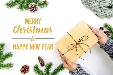 Christmas winter composition. Woman hand hold christmas gift box with pine cones, fir branches on white background. Flat lay, top view, copy spaceの写真素材
