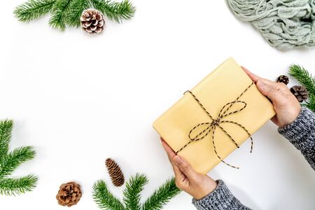 Christmas winter composition. Woman hand hold christmas gift box with pine cones, fir branches on white background. Flat lay, top view, copy spaceの写真素材