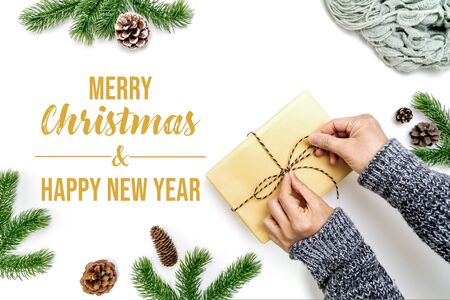 Christmas winter composition. Woman hands wrapping Christmas gifts box with pine cones, fir branches on white background. Flat lay, top view, copy spaceの写真素材