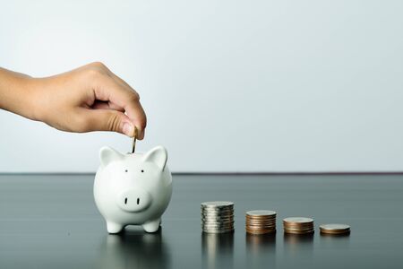 Money saving and donation concept, child put money on cute white piggy bankの写真素材