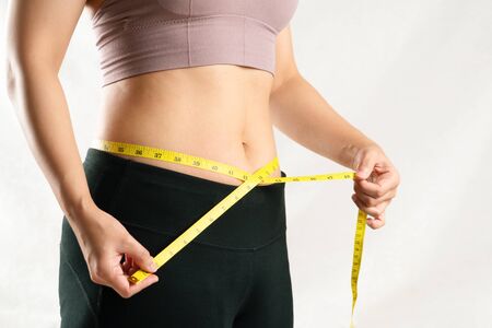 young woman measuring her belly waist with measure tape, woman diet lifestyle conceptの写真素材