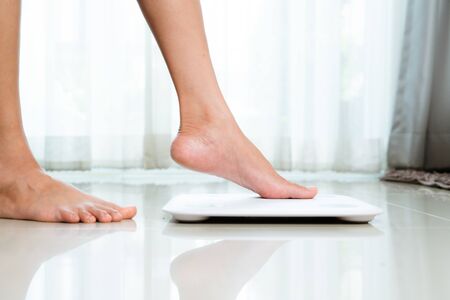 Female leg is stepping on white scales at homeの写真素材