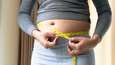 Fat woman hand holding measurement tape on her belly fat. woman diet lifestyle and build muscle concept.の写真素材