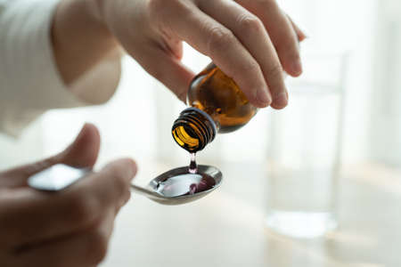 Woman hand pouring medication or cough syrup from bottle to spoon. healthcare conceptの写真素材