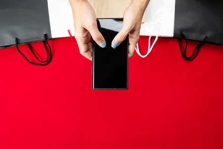black friday sale, woman hand online shopping on smartphone with shopping bag on red backgroundの写真素材