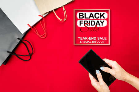 black friday sale, woman hand online shopping on smartphone with shopping bag on red backgroundの写真素材