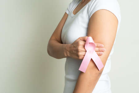 pink badge ribbon on woman hand touching chest to support breast cancer cause. breast cancer awareness conceptの写真素材