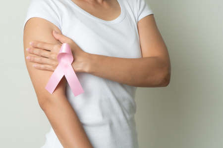 pink badge ribbon on woman hand touching chest to support breast cancer cause. breast cancer awareness conceptの写真素材