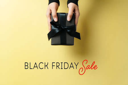 black friday sale, woman hand give the gift box on yellow backgroundの写真素材