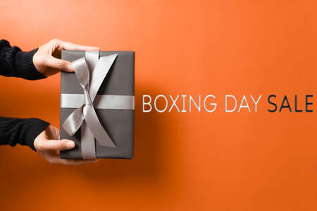 Boxing Day sale, young woman hand with a gift box offer to receiverの写真素材