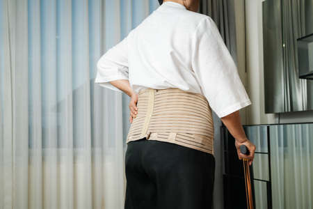 Senior back pain woman with walking stick at homeの写真素材