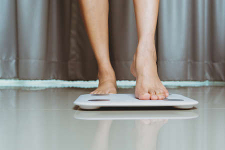 Female leg is stepping on white scales at homeの写真素材