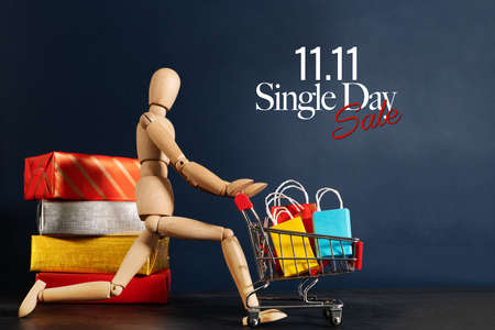11.11 singles day sale concept, shopaholic wooden doll with lots of shopping bags on arm and shopping cartの写真素材