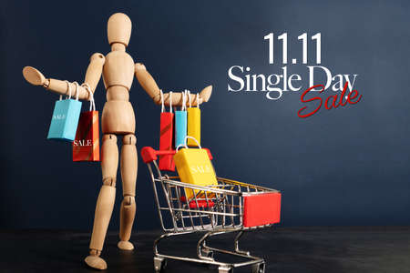 11.11 singles day sale concept, shopaholic wooden doll with lots of shopping bags on arm and shopping cartの写真素材