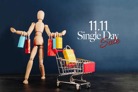 11.11 singles day sale concept, shopaholic wooden doll with lots of shopping bags on arm and shopping cartの写真素材