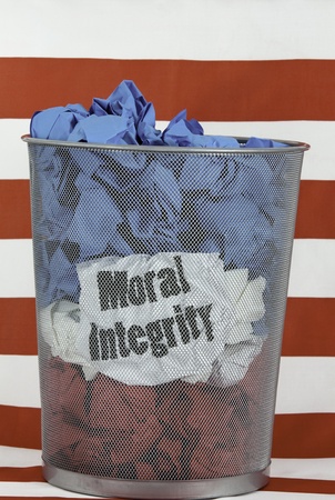 Politics and Moral Integrity. Waste basket with wads of red, white, and blue paper, The words MORAL INTEGRITY show through the wastebasket. Red and white striped background.の写真素材