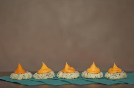 Five thumbprint cookies in a row with orange icing sitting on green napkins against a stucco background  Selective focus の写真素材