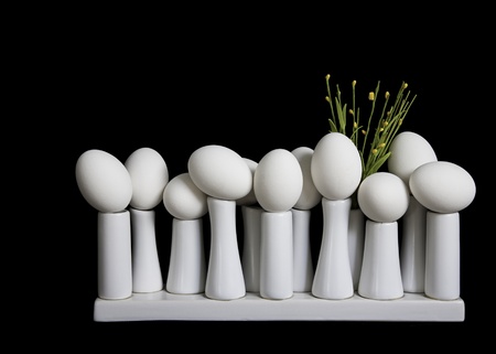 On the Edge  Eggs carefully positioned on small white pedestals with yellow flowers against black background   の写真素材