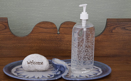  Clear Hand Sanitizer placed on unique plates on vintage oak hall table with welcome sign against...