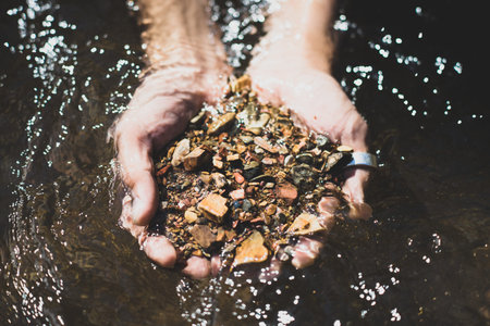 Man hands holding brown pebbles against river in the background. Vintage style photo.