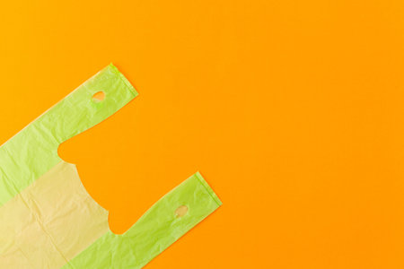 Flat lay photo of green plastic bag from supermarket on orange background with copy space for zero...
