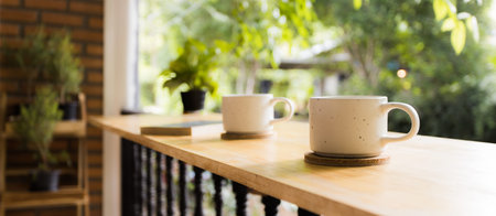 Panoramic photo of close up two ceramic coffee cups on wooden bar terrace in peaceful day time at home. Romantic greenery atmosphere.の写真素材