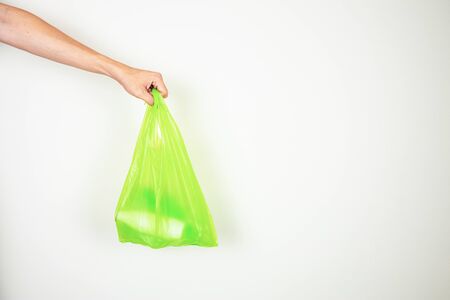 One hand holding supermarket green plastic bag containing plastic bottle inside. Shot on white background with copy space.の写真素材