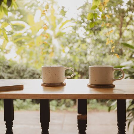 A book and two ceramic coffee cups on wooden terrace in peaceful day time at home in Asia with romantic greenery atmosphere background, close up shot.の写真素材