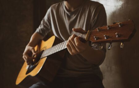 An asian male musician playing acoustic guitar solo finger style picking in room corner.の写真素材