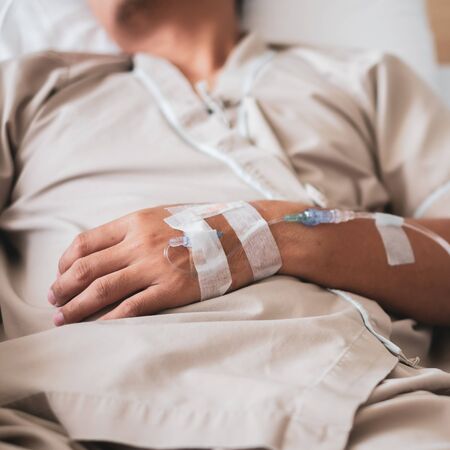 Close up sick asian man lying in bed with injection needle stick on hand during medical procedure and infusion to recovery in hostpital.の写真素材