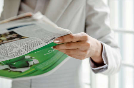 Businesswoman reading newspaper in front of windowの写真素材
