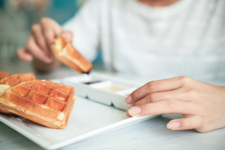 close up of woman holding a waffle and dip into sauceの写真素材