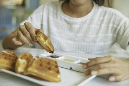 woman holding a waffle and dip into sauceの写真素材