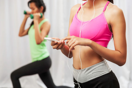 close up of woman using to her phone while another woman exercising