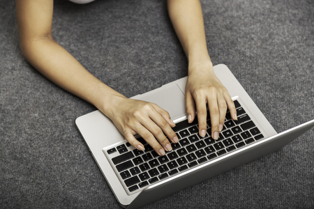 top view of a young woman laying on the floor while using her laptopの写真素材