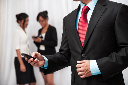 businessman using his mobile phone while two women are talking in the backgroundの写真素材