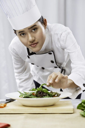 portrait of female chef patiently placing salad on a plateの写真素材