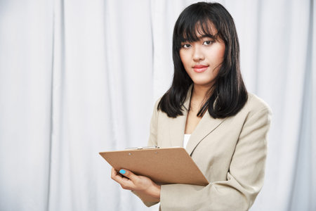 close up of businesswoman wearing beige suit standing and taking note on folderの写真素材