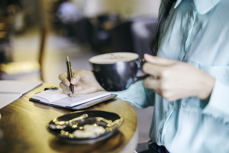 woman in holding a cup of cappuccino while writingの写真素材