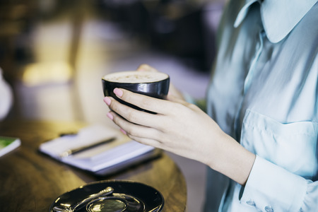 woman in blue shirt holding a cup of cappuccinoの写真素材