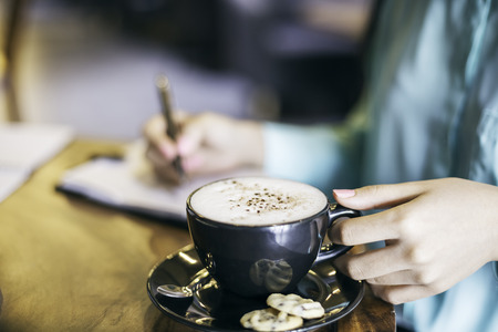 woman in holding a cup of cappuccino while writingの写真素材