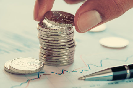 Holding a coin over Singapore coins and financial chart and ballpoint pen