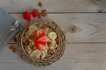 Oatmeal porridge with strawberries and nuts on light wooden backgroundの写真素材